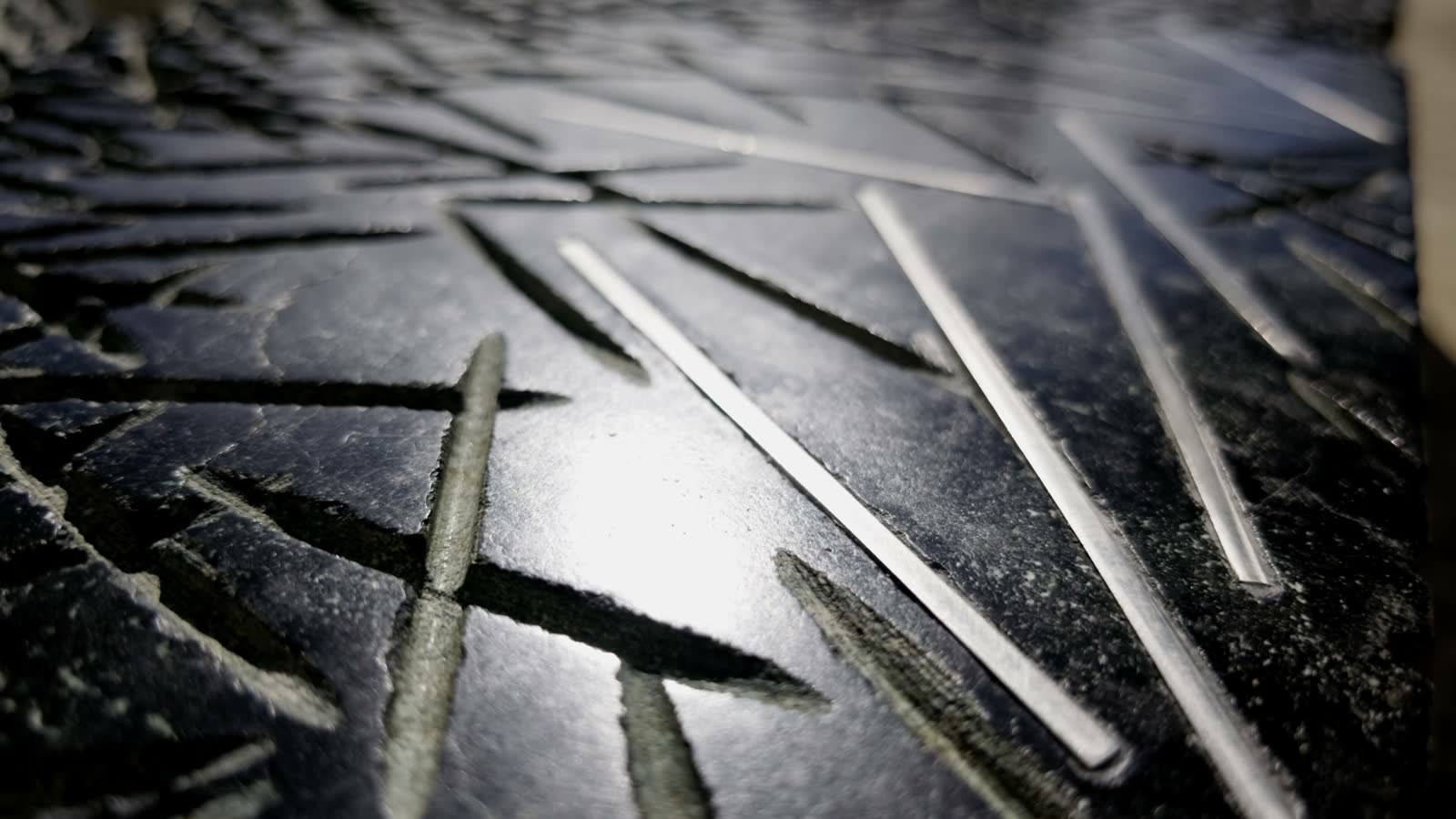 Nahaufnahme der dunklen Steinoberfläche mit kreuz und quer verlaufenden Einschnitten; einige davon glänzen silbern, sie sind mit Edelstahl ausgelegt.
